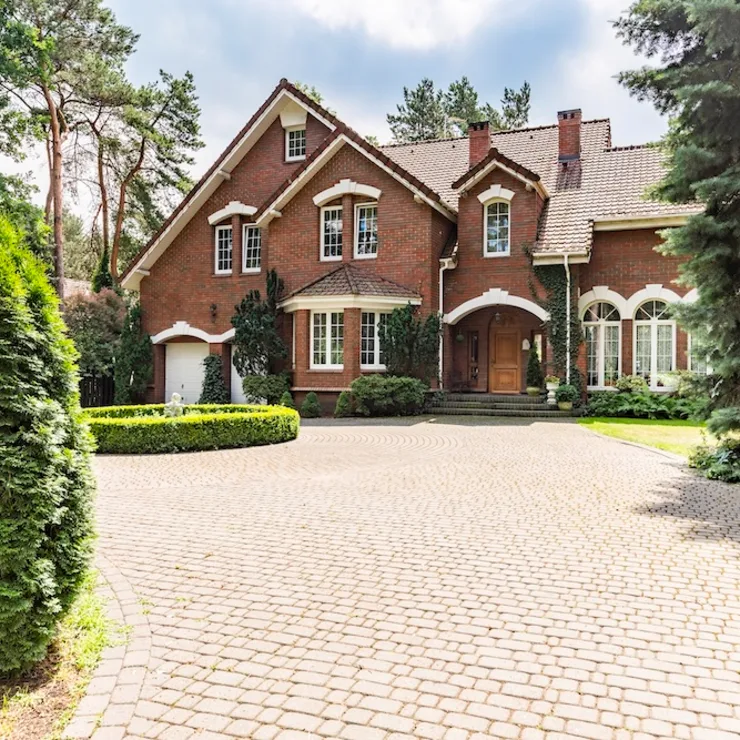 Großes Backsteinhaus mit Einfahrt, umgeben von Bäumen und gepflegtem Garten.
