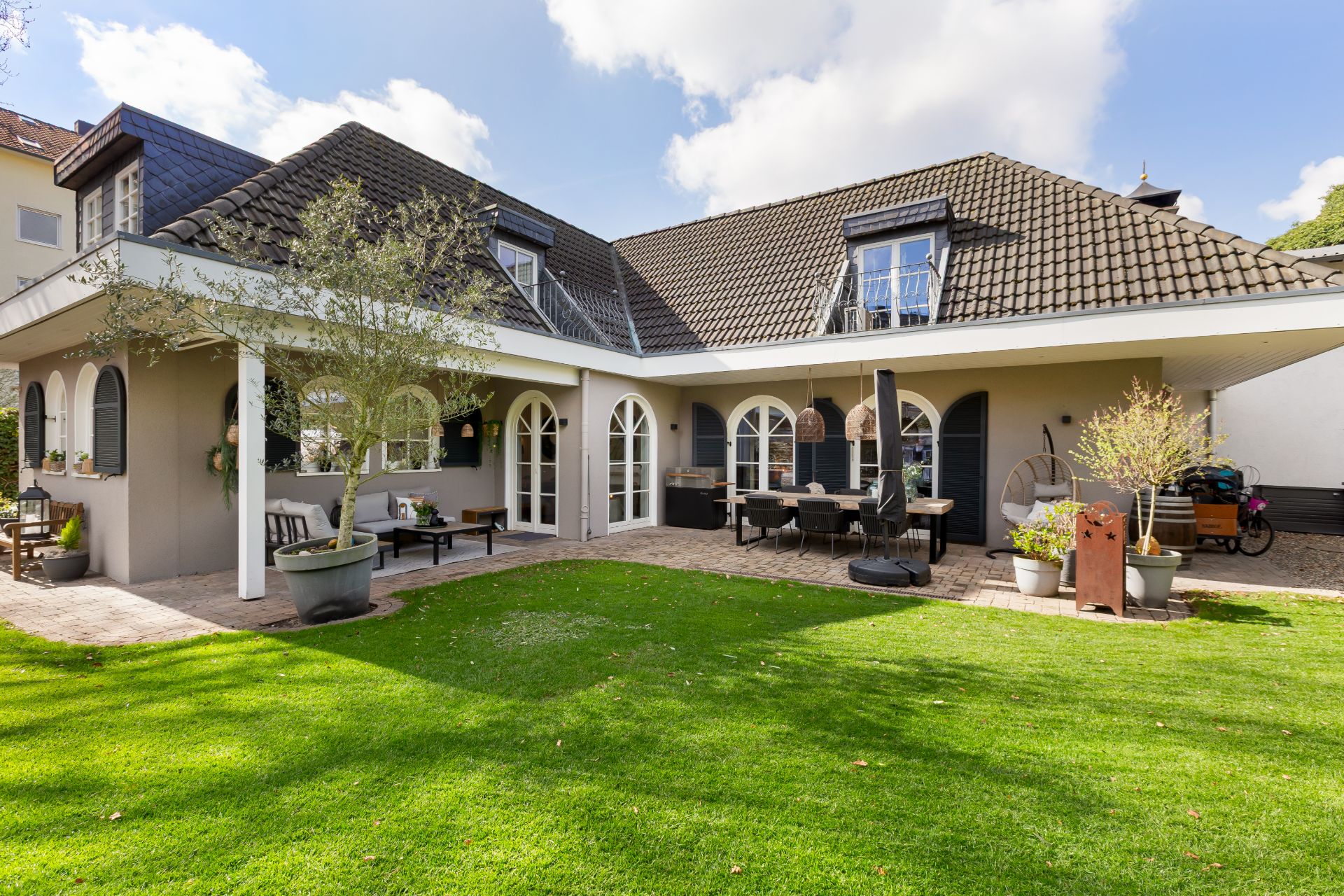 Haus mit überdachter Terrasse, Rasenfläche und Sitzbereich im Garten.