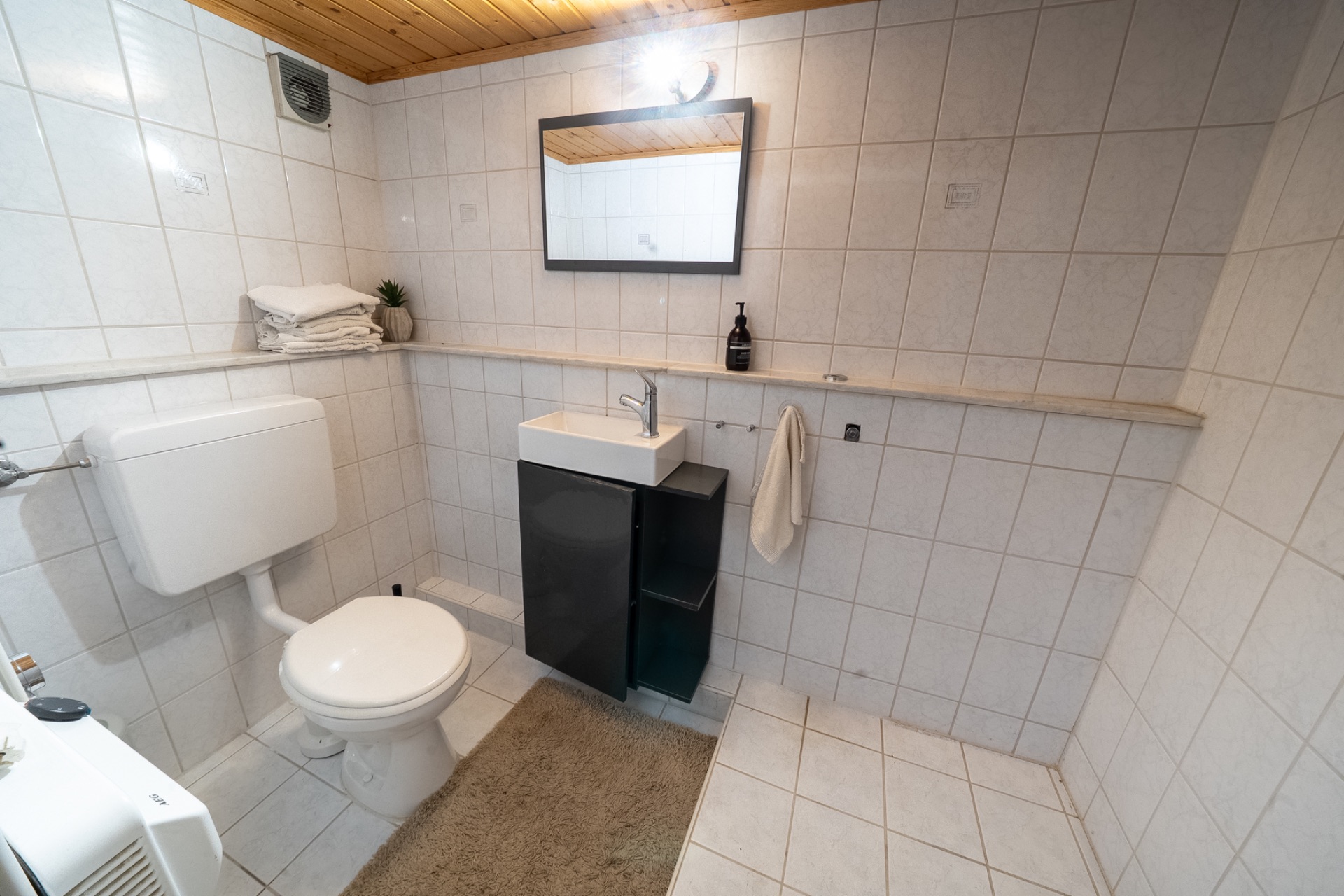 Helles Badezimmer mit WC, Waschbecken, Spiegel, Handtuch und gefliestem Boden.