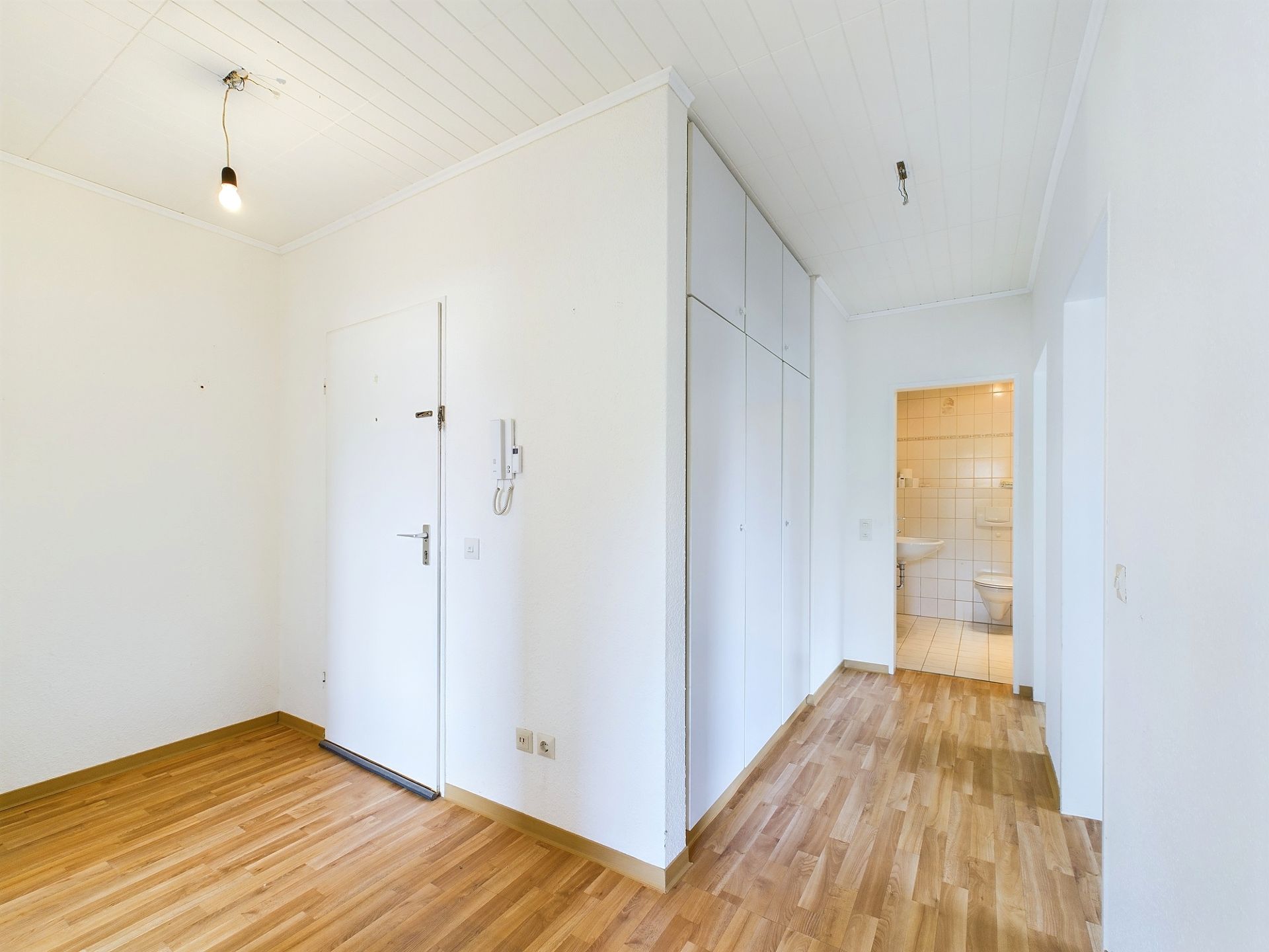 Heller Flur mit Holzboden, weißer Tür, Einbauschrank und Zugang zu einem Badezimmer.