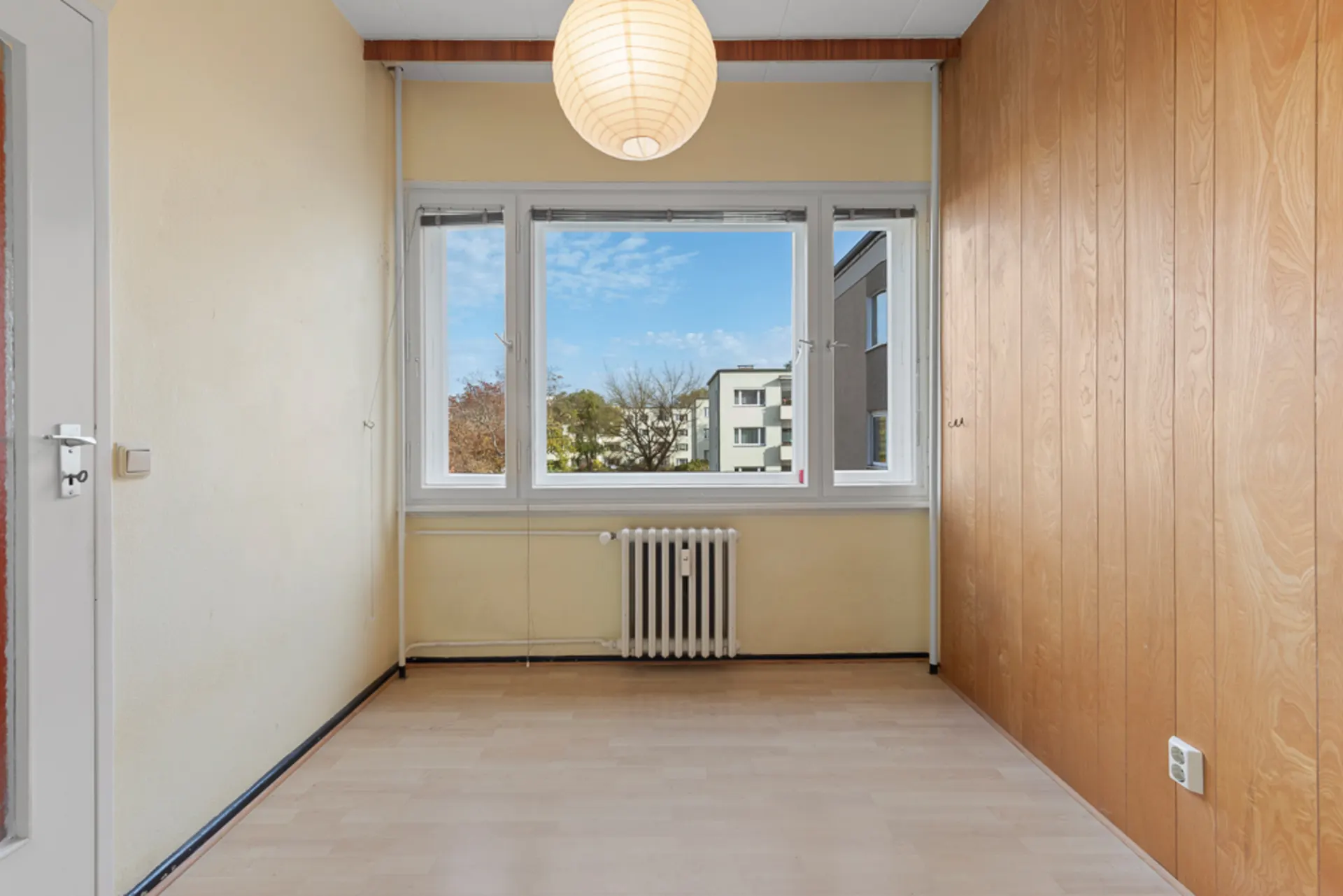 Kleiner leerer Raum mit Holzvertäfelung, großem Fenster und Deckenleuchte.