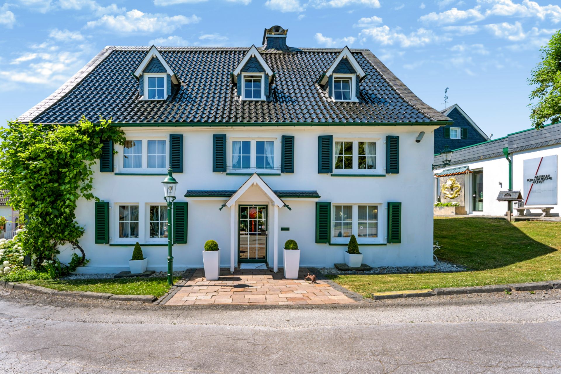 Weißes Wohnhaus mit grünem Dach, grünen Fensterläden und gepflegtem Vorgarten.