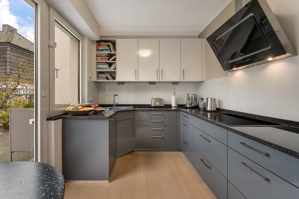 Moderne Küche mit grauen Unterschränken, weißen Hängeschränken und Blick auf einen Balkon.