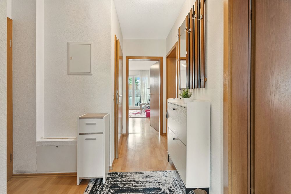 Heller Flur mit Holzboden, Garderobe, Schuhschrank und Blick in ein Wohnzimmer.