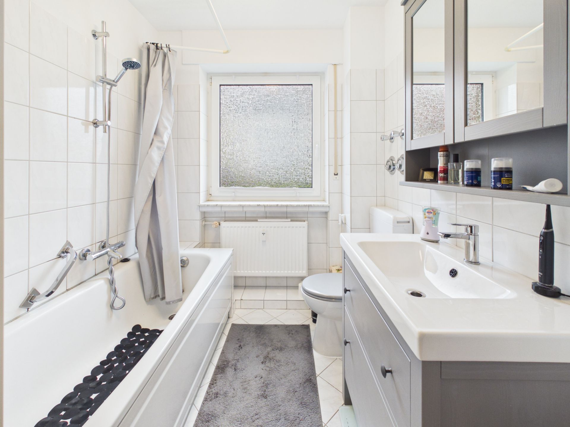 Helles Badezimmer mit Badewanne, Waschbecken, Spiegel und Fenster.