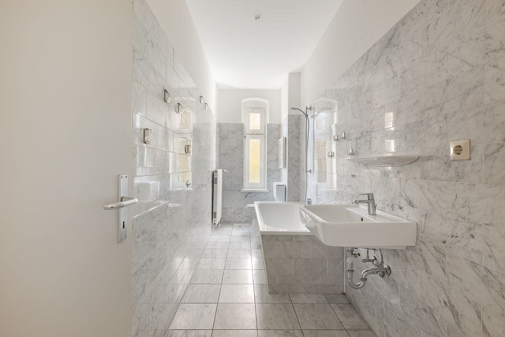 Helles Badezimmer mit Badewanne, Waschbecken, WC und gefliesten Wänden.
