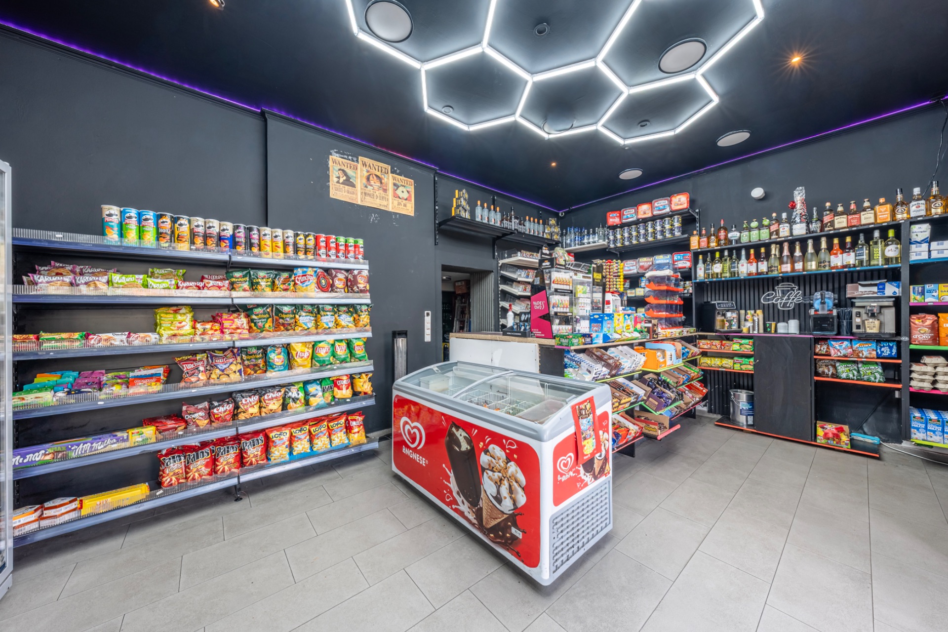 Kleiner Laden mit Regalen voller Snacks, Getränken und einer Eistruhe in der Mitte.