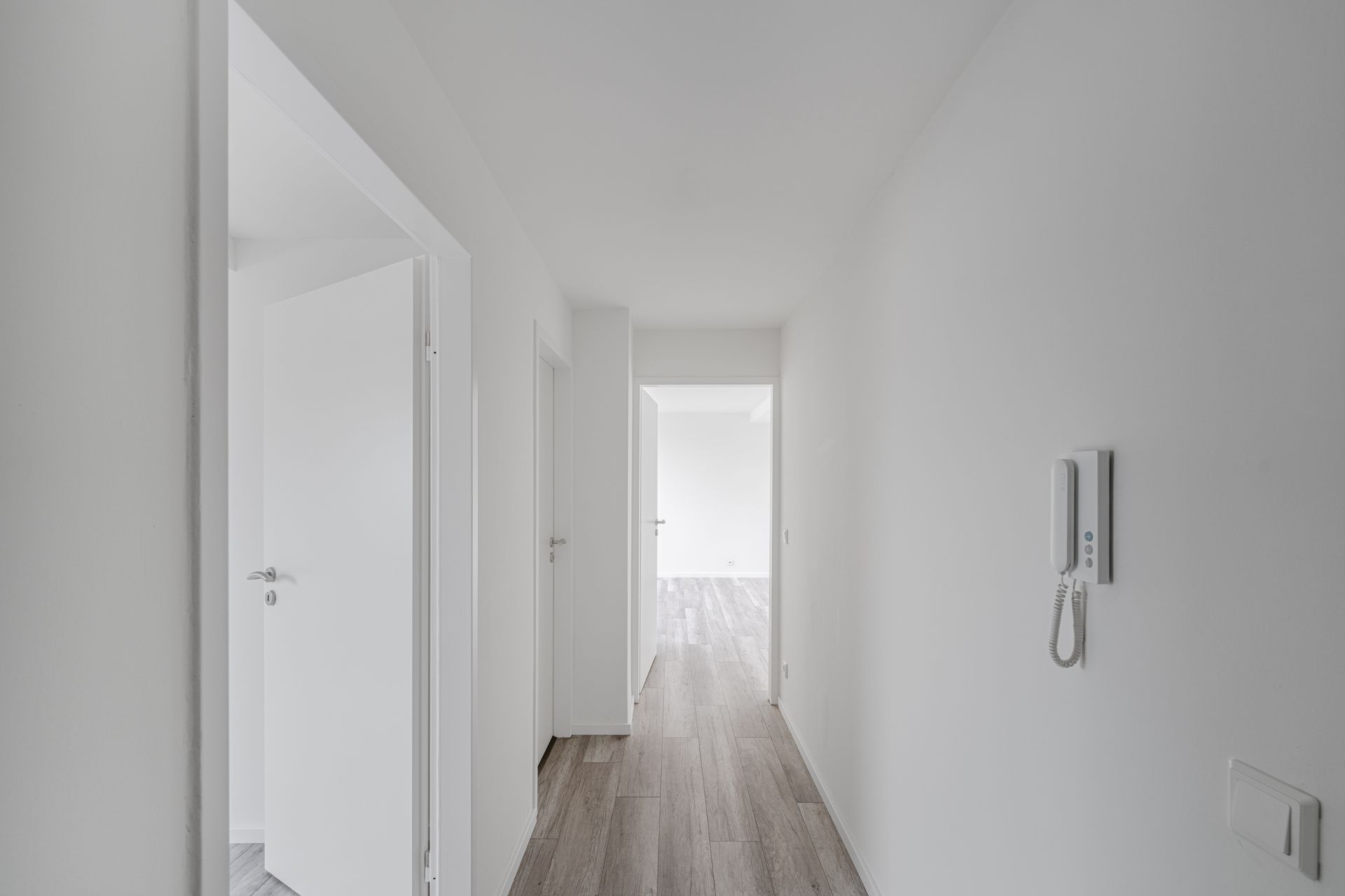 Heller Flur mit Holzboden, weißen Türen und Gegensprechanlage an der Wand.
