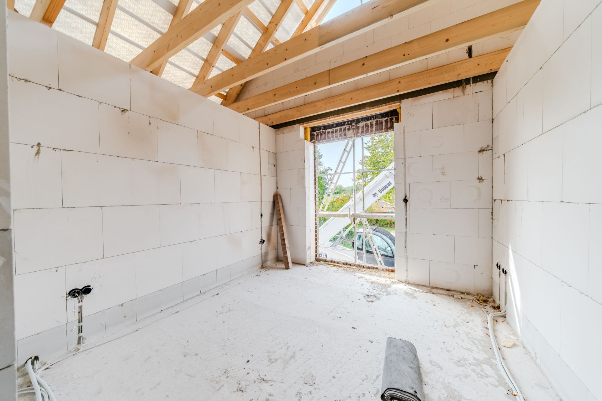 Heller Raum im Rohbau mit sichtbarem Holzgebälk und offenem Fensterbereich.