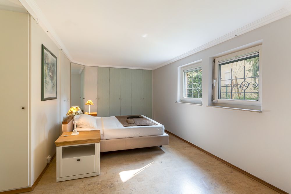 Helles Schlafzimmer mit Doppelbett, Nachttisch, Lampen, Einbauschrank und zwei Fenstern.