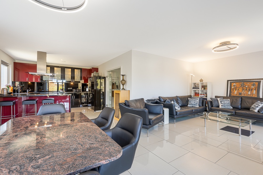 Modernes Wohnzimmer mit schwarzem Sofa, Essbereich und offener Küche mit roten Schränken.