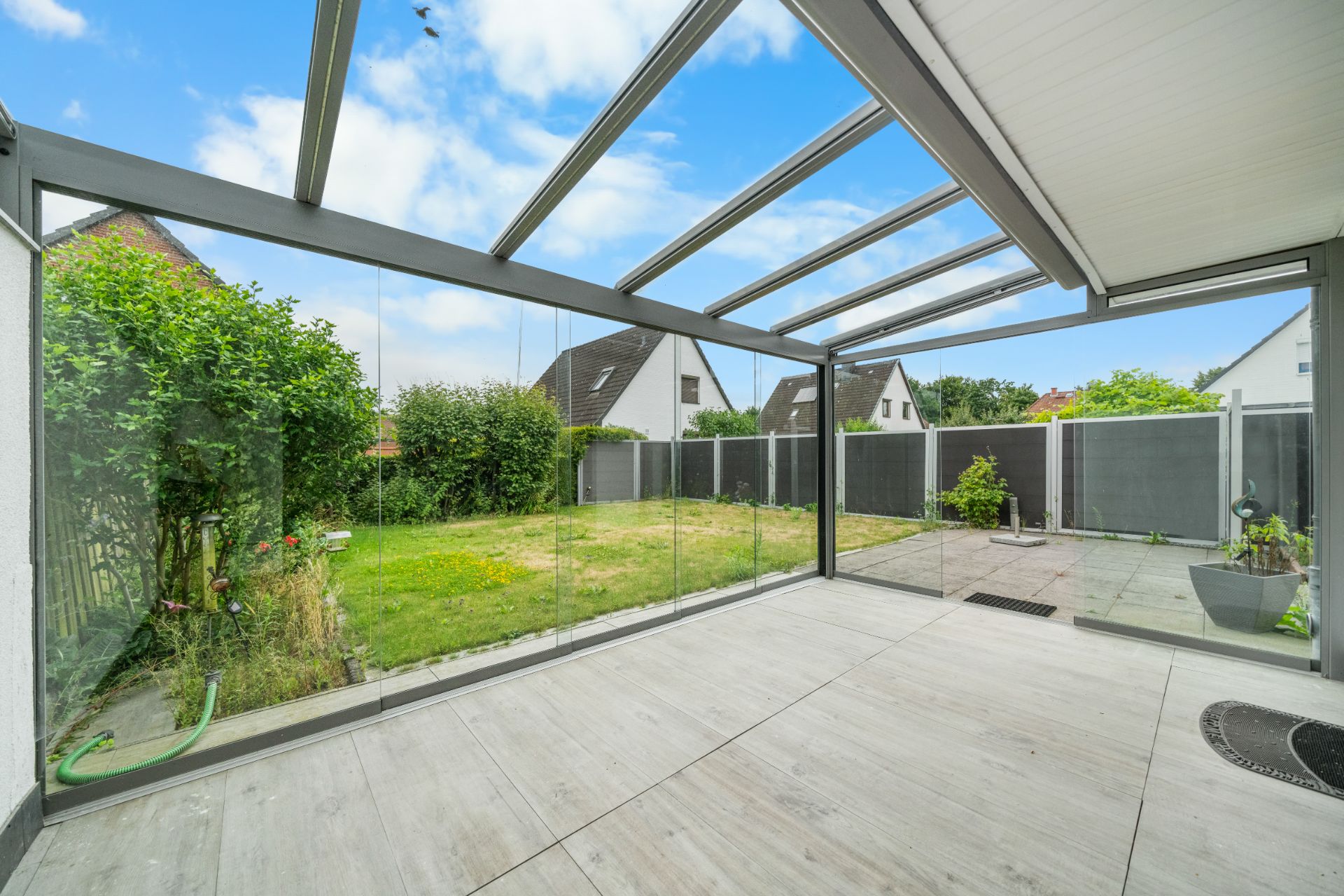 Überdachte Terrasse mit Glaswänden, Blick auf Garten und angrenzenden Rasen.