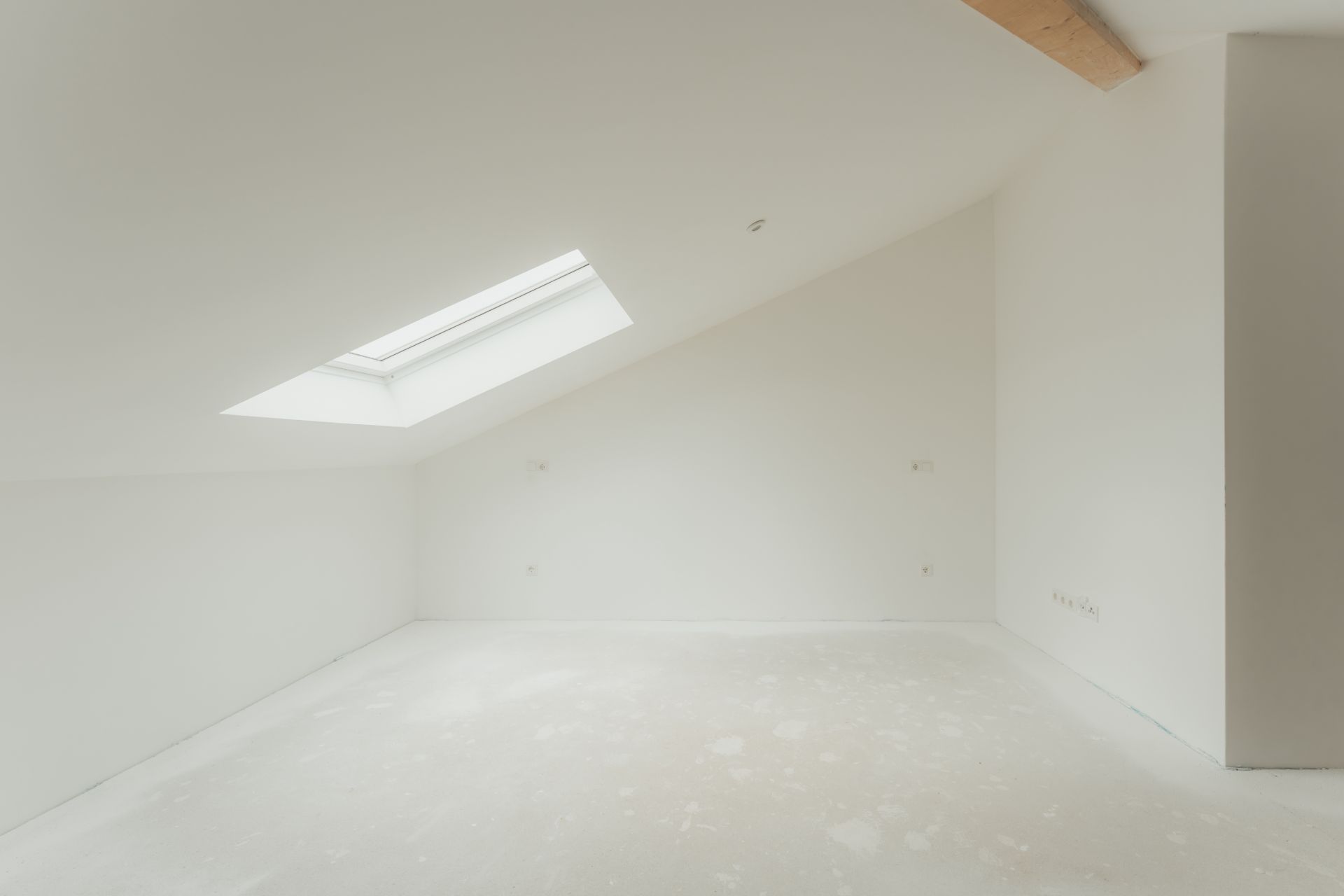 Heller leerer Raum mit schräger Decke und großem Dachfenster.