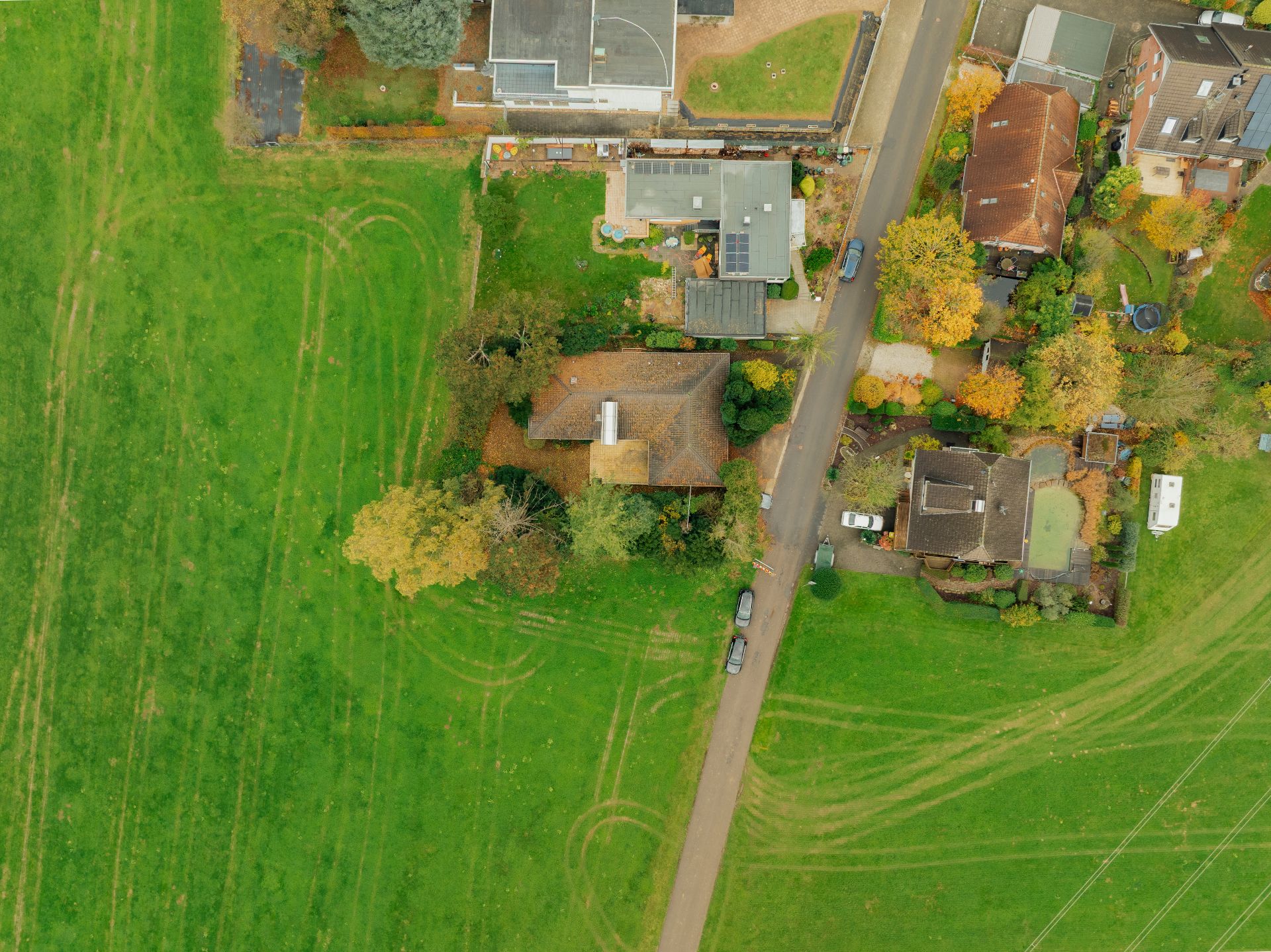 Luftaufnahme von Häusern und Gärten an einer Straße neben einer großen grünen Wiese.