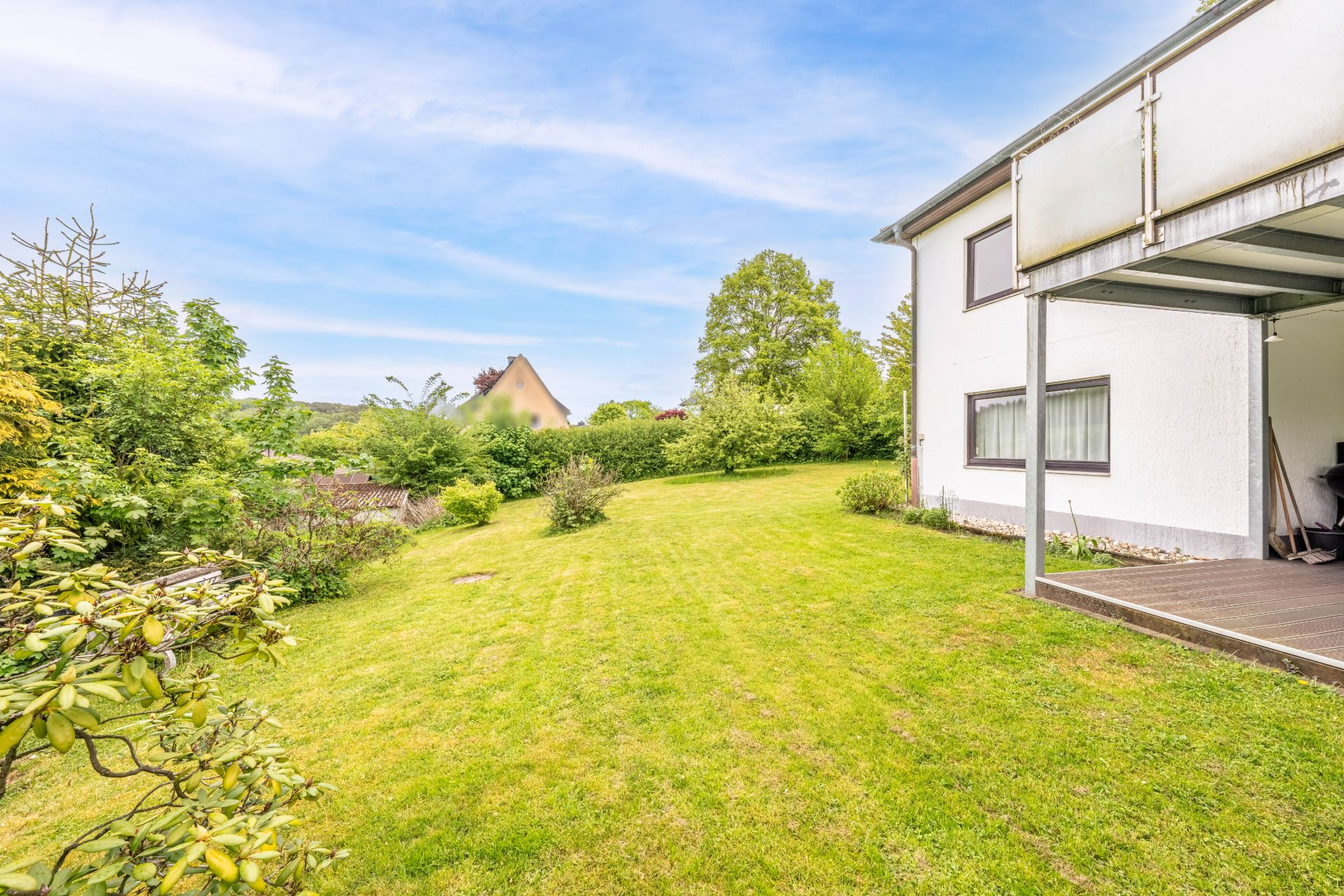 Grüner Garten mit Rasenfläche neben einem weißen Wohnhaus und Terrasse.
