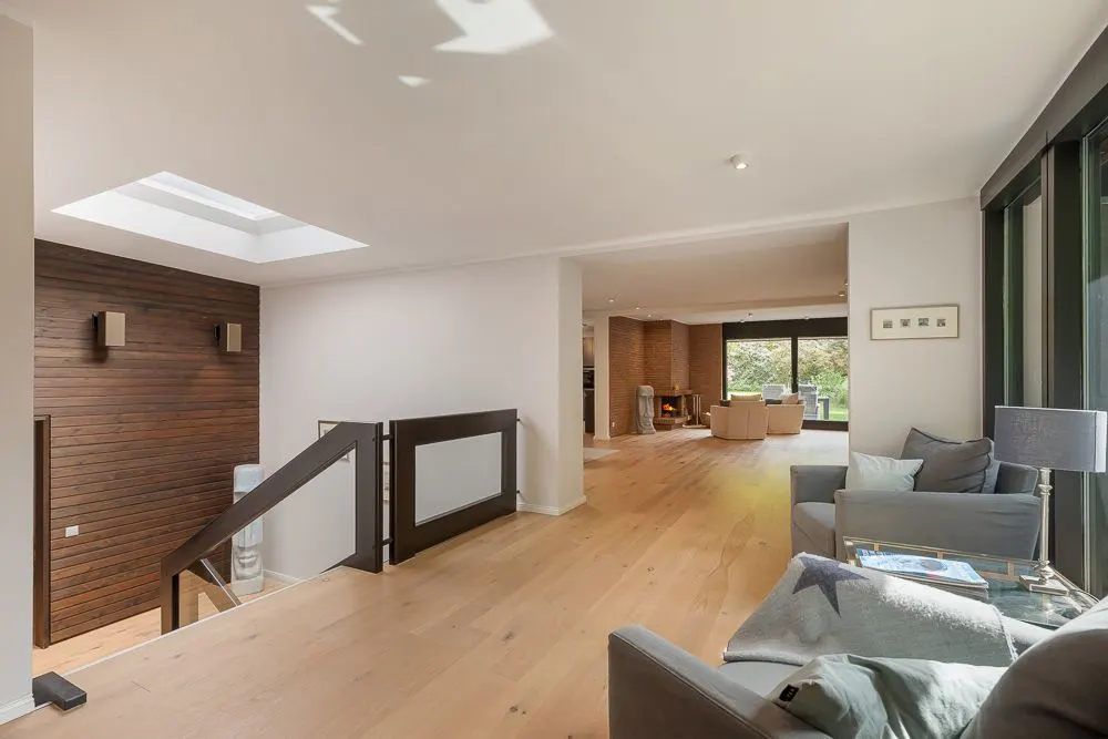 Helles Wohnzimmer mit Holzboden, Sofas, großen Fenstern und Zugang zu einer Treppe.