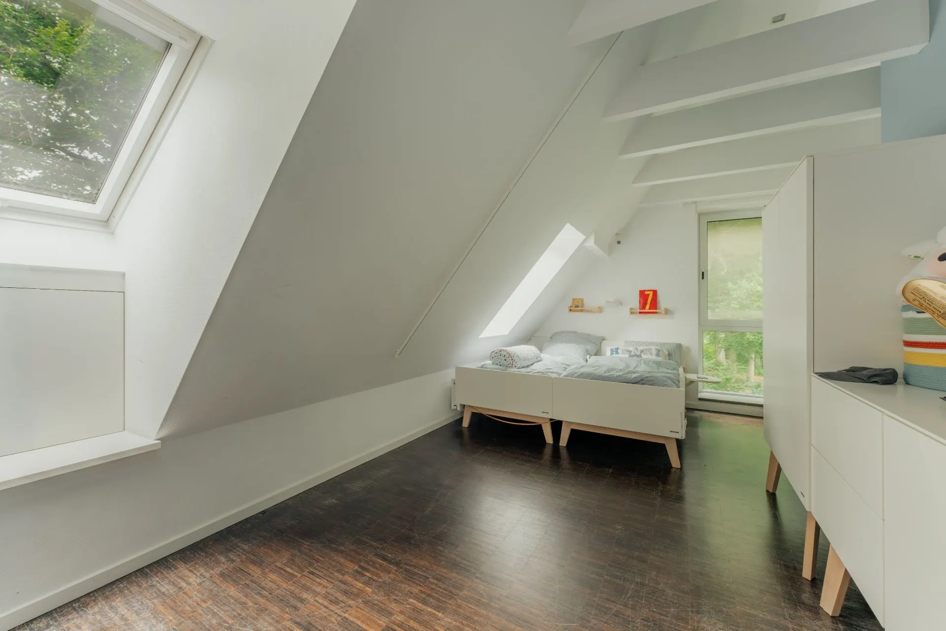 Helles Schlafzimmer mit Dachschräge, Bett, Fenster und dunklem Holzboden.