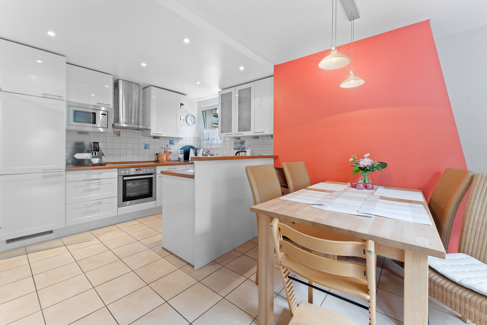 Moderne Küche mit Esstisch, vier Stühlen und rosafarbener Wand im Hintergrund.