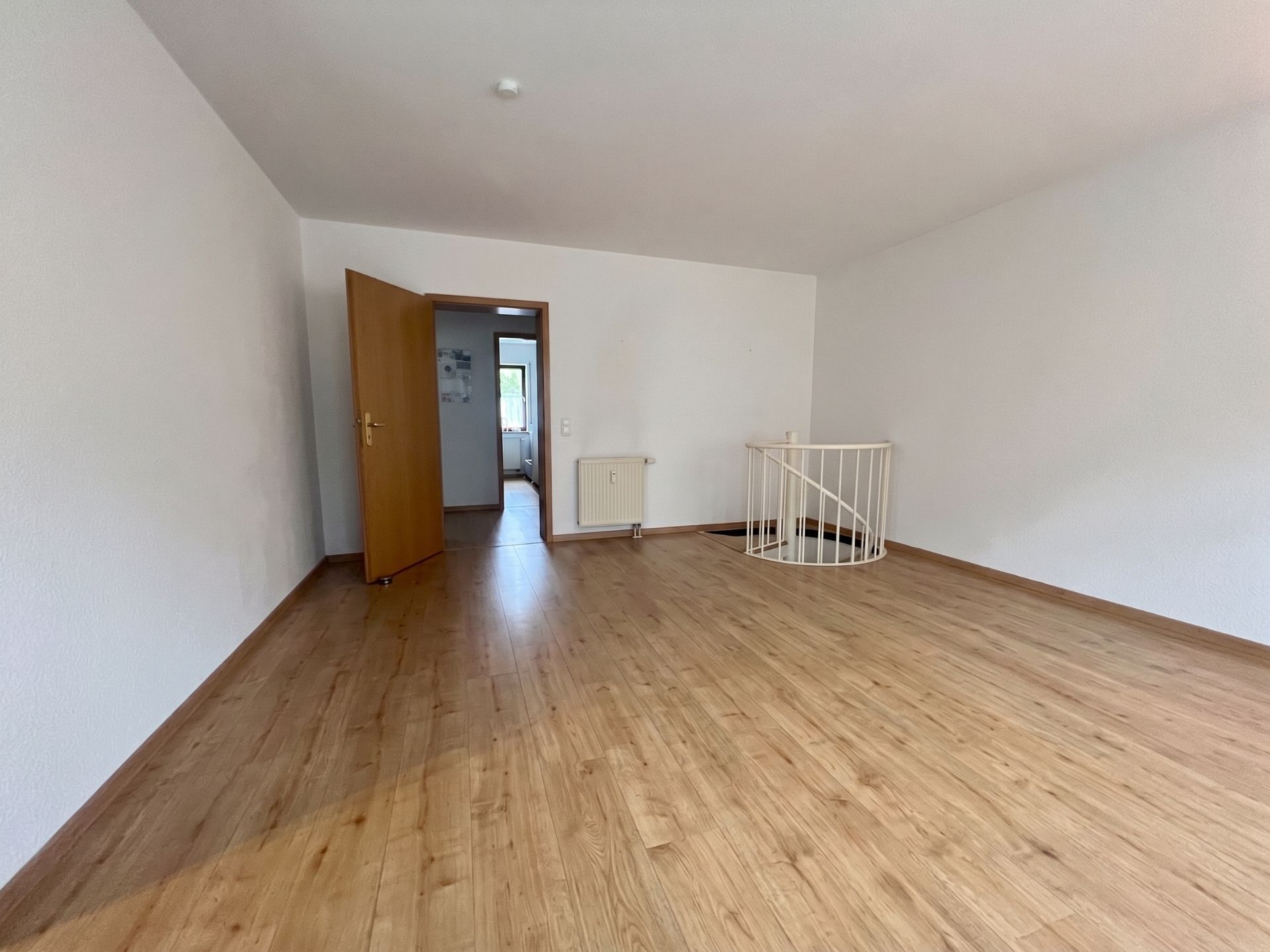 Leerer Raum mit Holzboden, offener Tür und Treppe mit weißem Geländer.