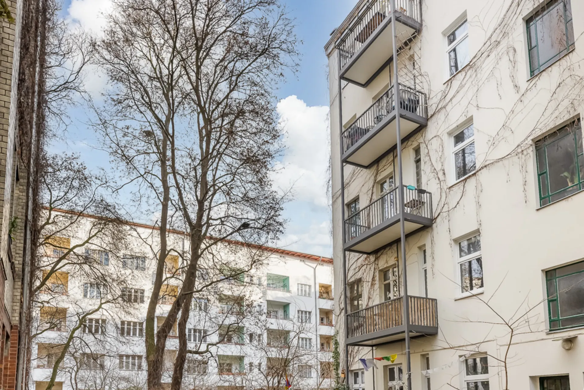 Mehrstöckiges Wohnhaus mit Balkonen, kahlen Bäumen und gegenüberliegendem Gebäude im Hof.