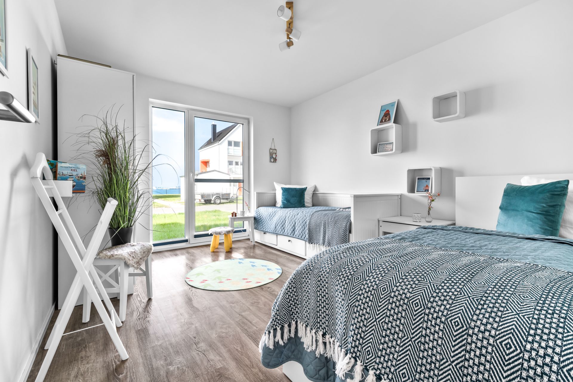 Helles Schlafzimmer mit zwei Betten, großen Fenstern, Holzboden und modernem Dekor.