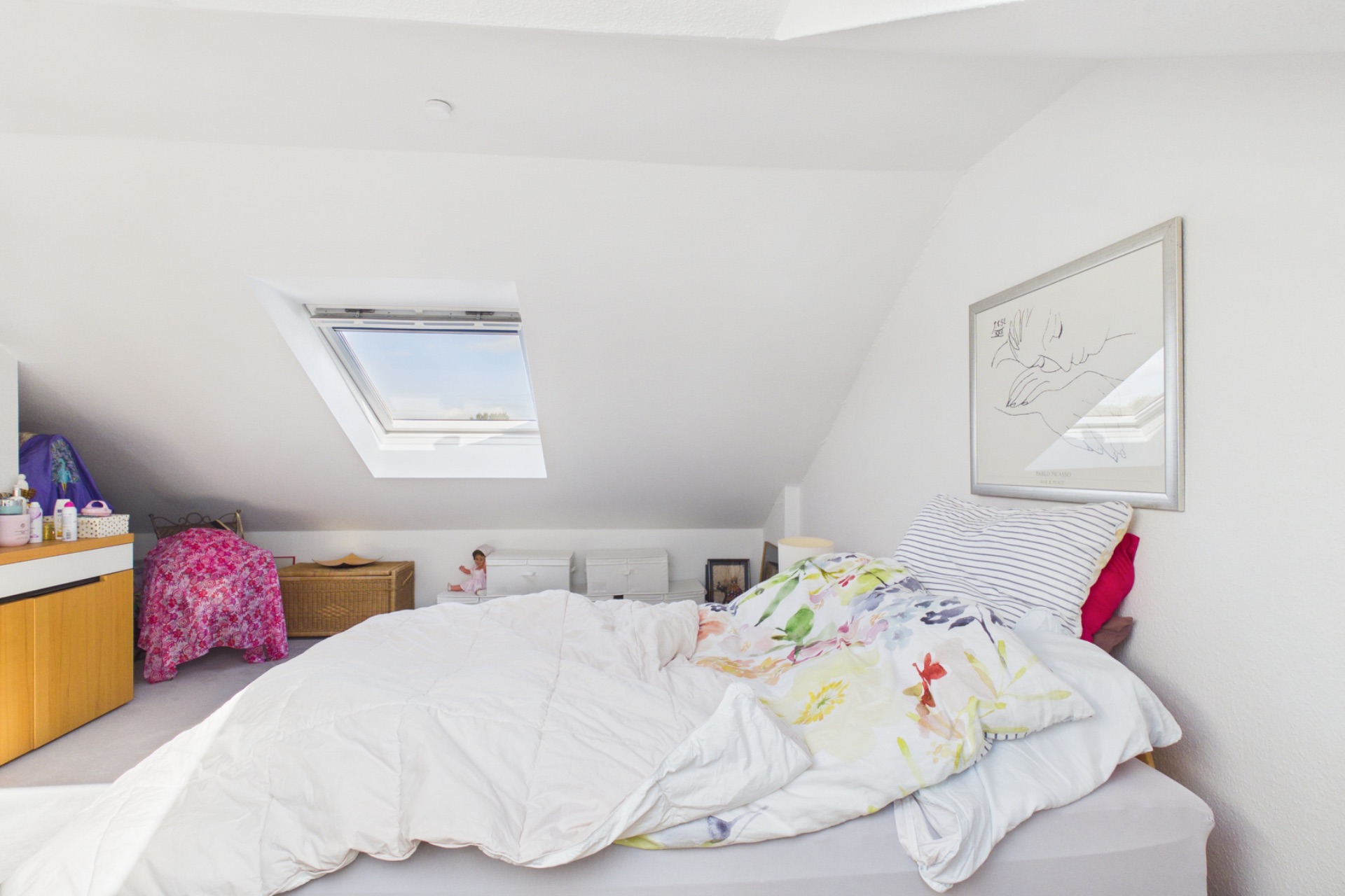 Helles Schlafzimmer mit Dachschräge, Bett, Dachfenster und Kommode.