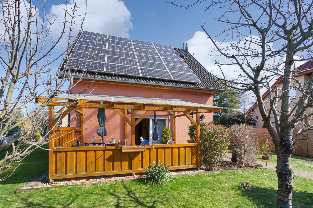 Haus mit Solarpanelen auf dem Dach und einer überdachten Holzterrasse im Garten.
