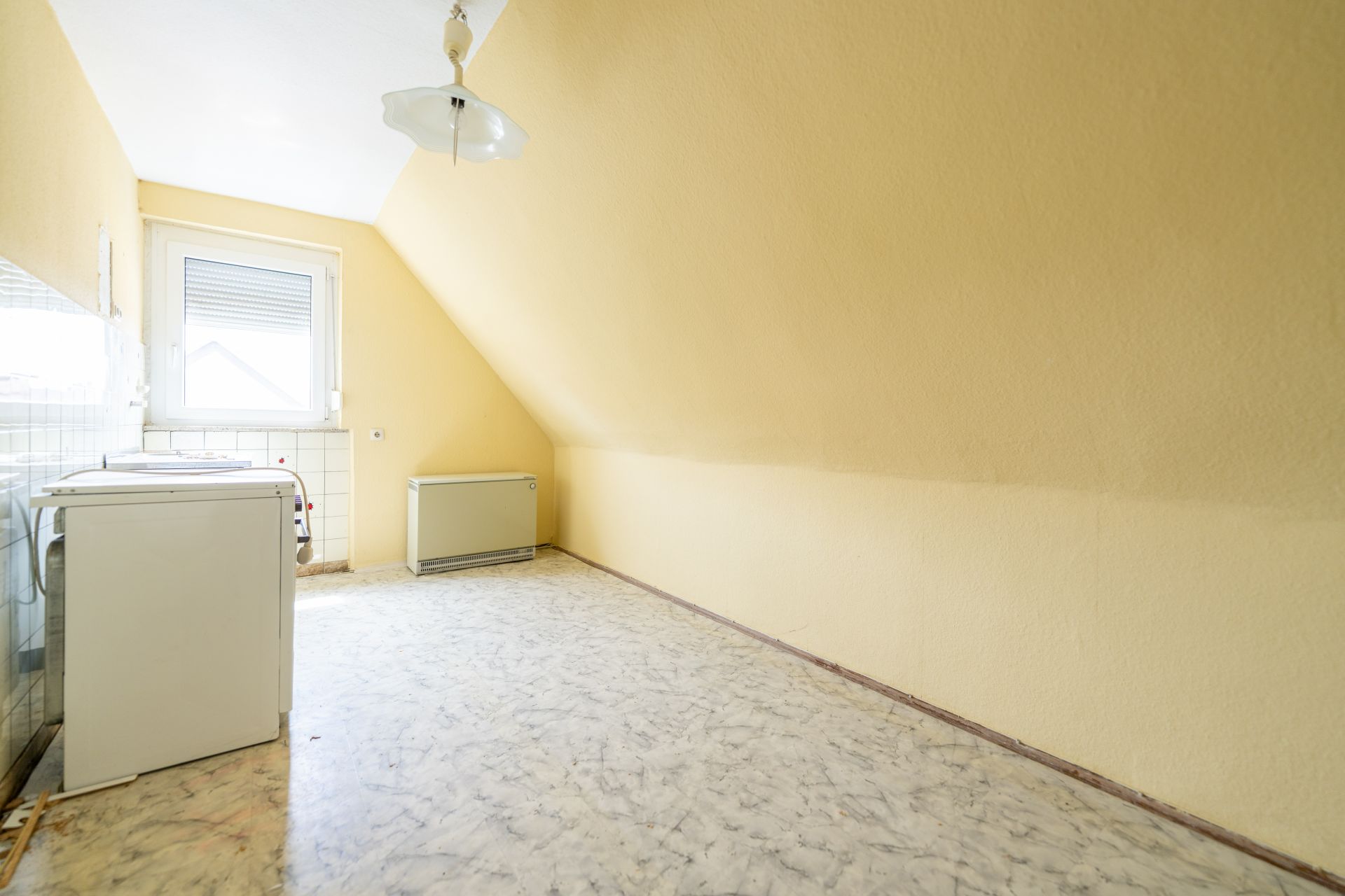 Heller Raum mit schräger Decke, zwei Haushaltsgeräten und einem Fenster.
