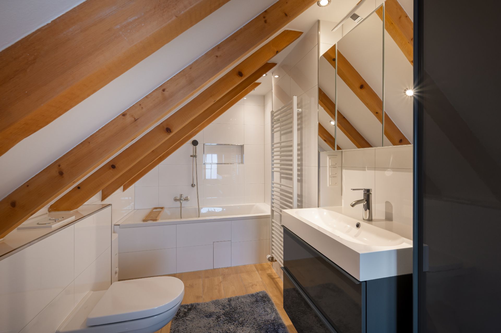 Modernes Bad mit sichtbaren Holzbalken, Badewanne, Waschbecken und Toilette unter einer Dachschräge.