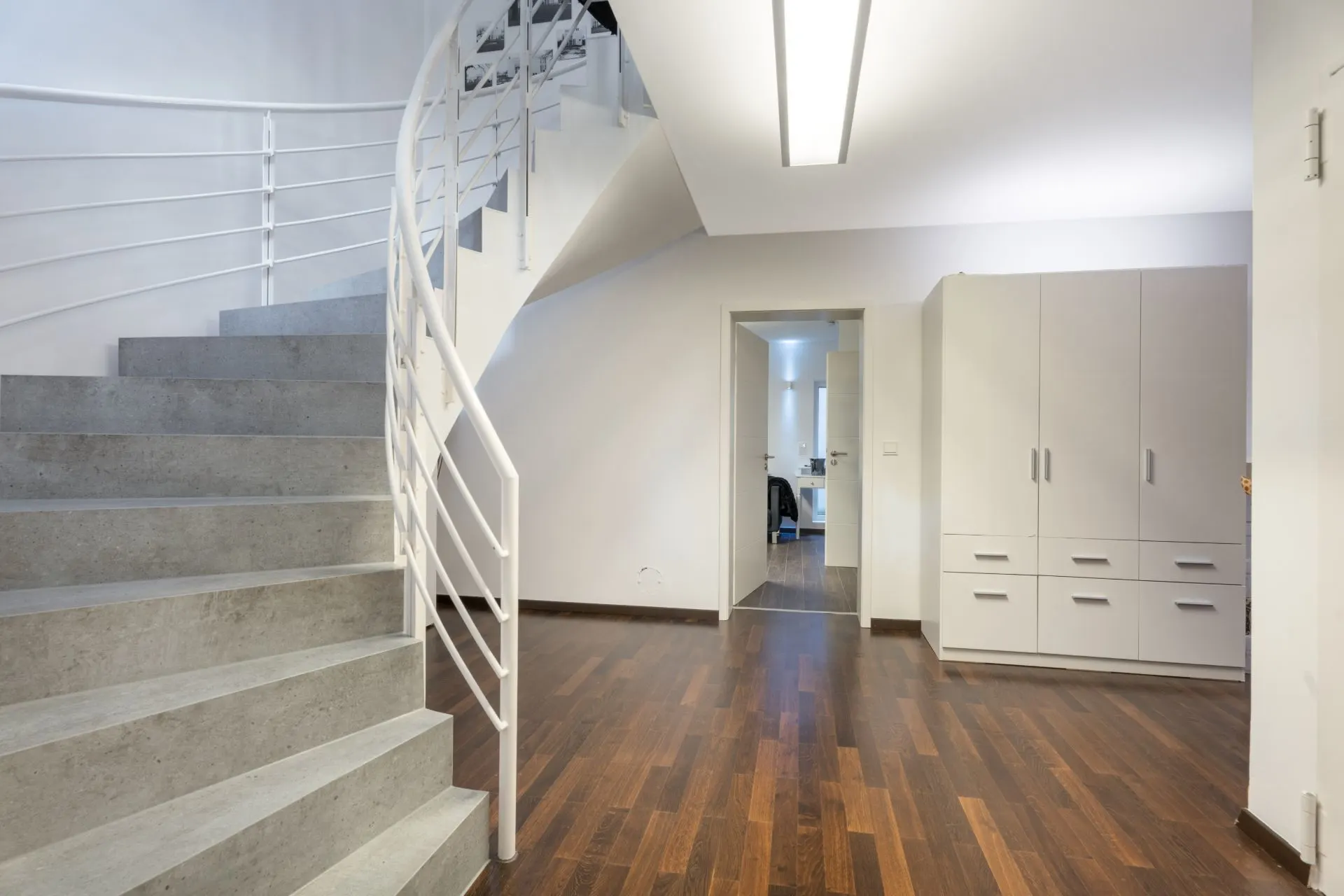 Moderner Flur mit Holzfußboden, grauer Treppe und weißem Wandschrank.