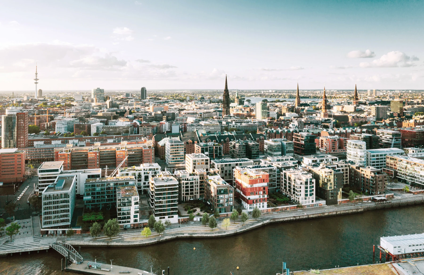 Luftaufnahme einer Stadt mit modernen Wohngebäuden und einem Fluss im Vordergrund.