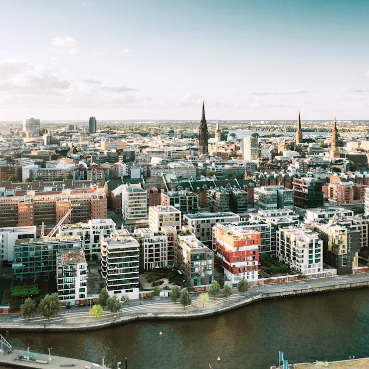 Luftaufnahme einer Stadt mit modernen Wohngebäuden und einem Fluss im Vordergrund.