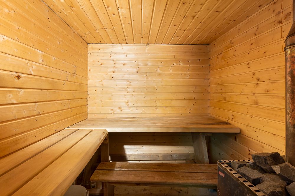 Holzverkleideter Saunaraum mit zwei Holzbänken und einem Saunaofen mit Steinen.