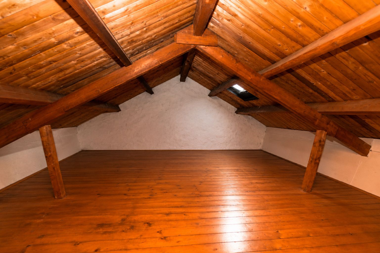 Dachboden mit Holzdecke und Holzboden, sichtbaren Balken und kleinem Fenster.