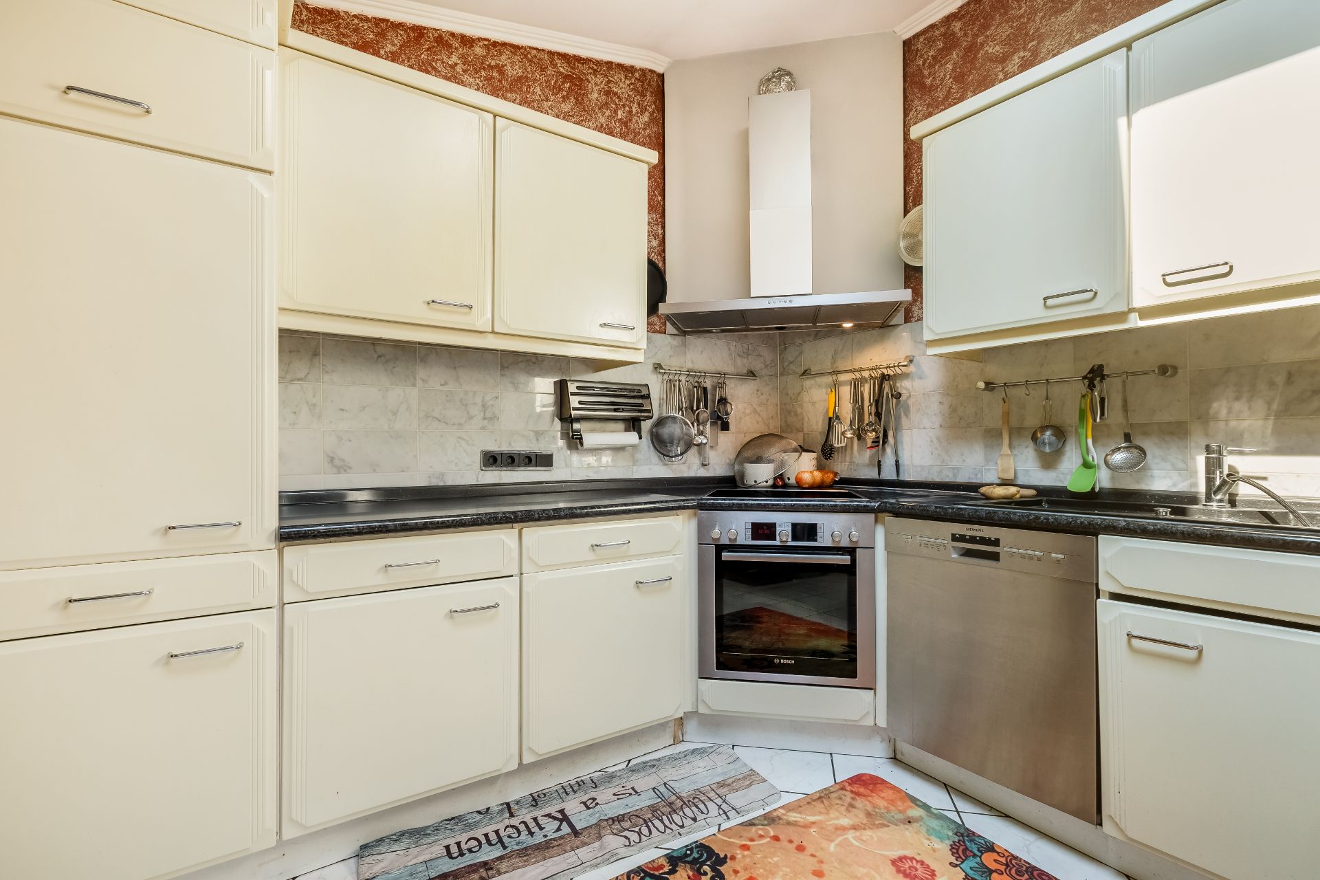 Helle Einbauküche mit Backofen, Spülmaschine, Hängeschränken und Küchenutensilien an der Wand.