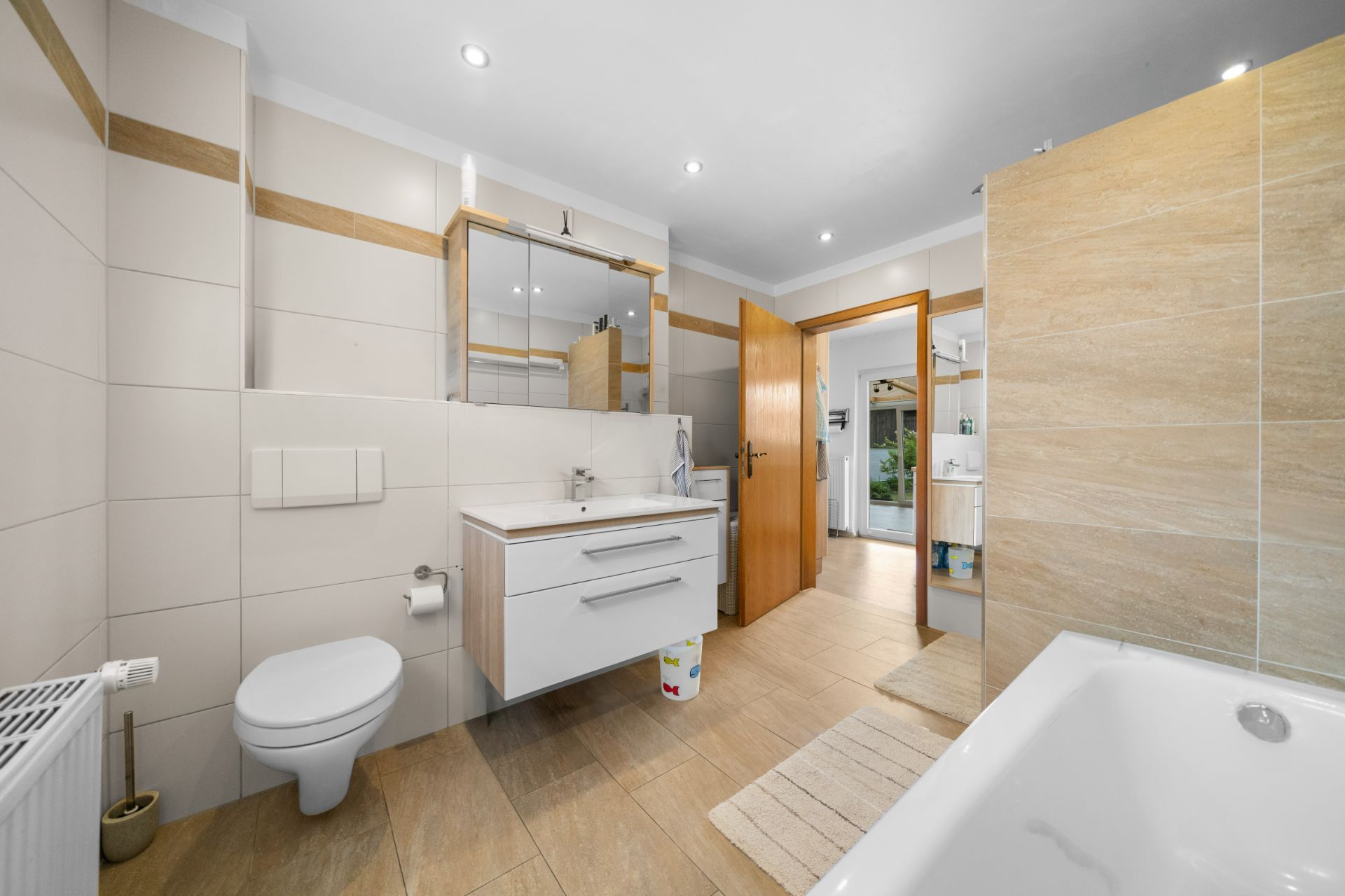 Modernes Badezimmer mit Badewanne, WC, Waschbecken und Spiegel, hell gefliest.