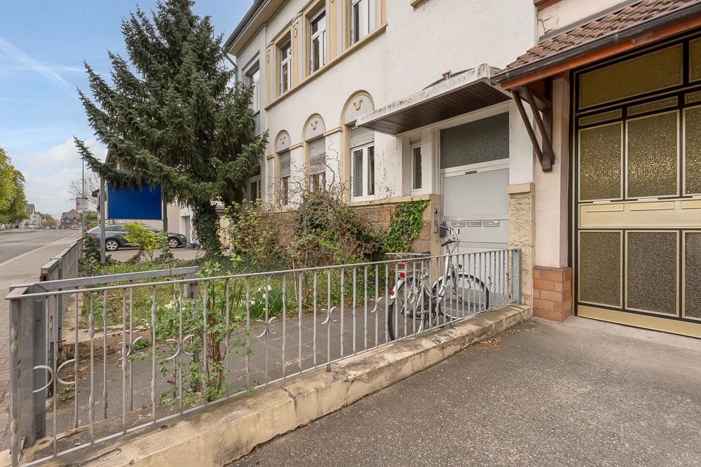 Vorgarten eines Wohnhauses mit Fahrrad, Zaun und kleinen Pflanzen neben einem Gehweg.