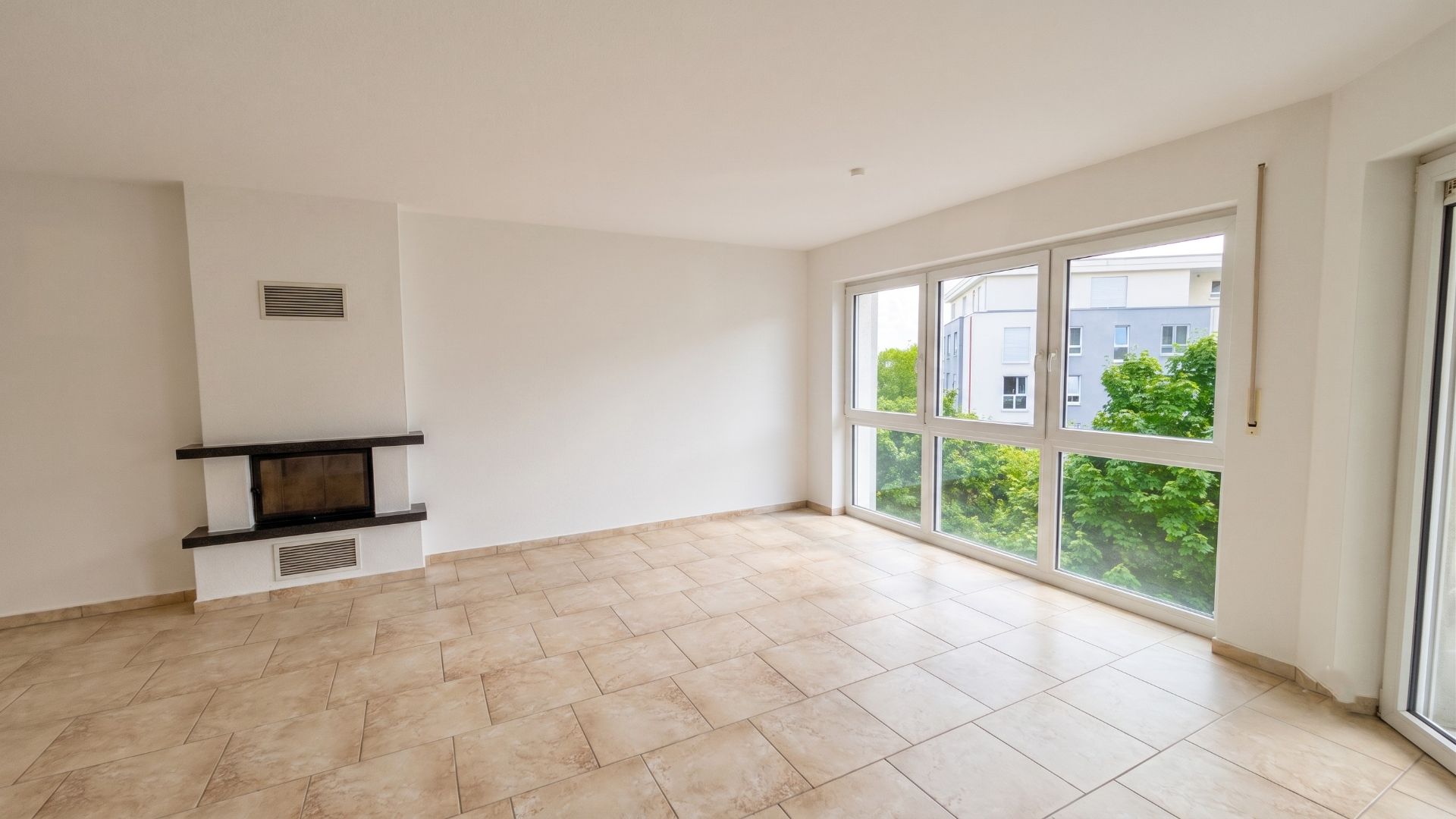 Helles Wohnzimmer mit großen Fenstern, Kamin und gefliestem Boden.