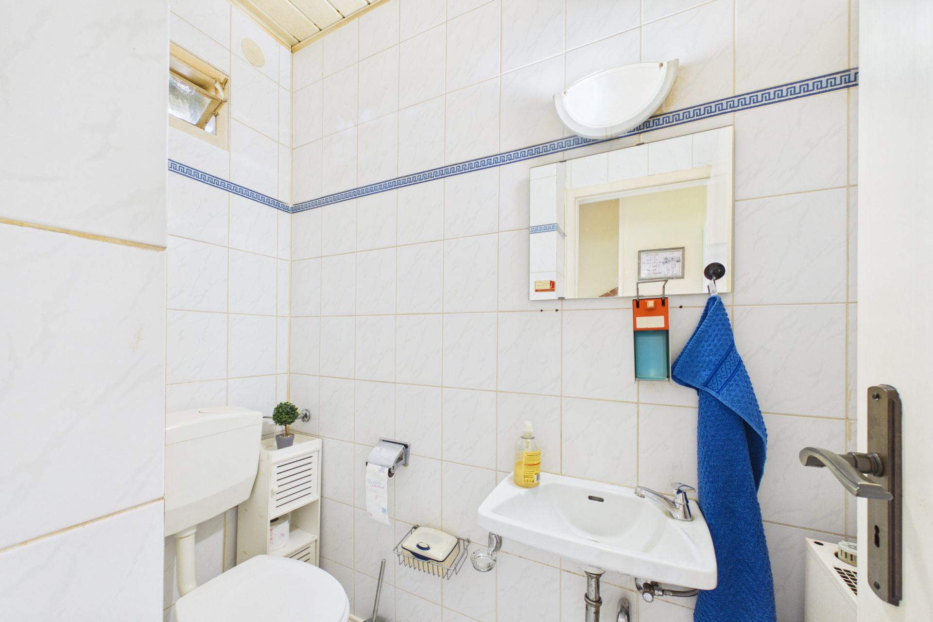 Kleines Badezimmer mit Waschbecken, Spiegel, Toilette und blauem Handtuch an der Wand.