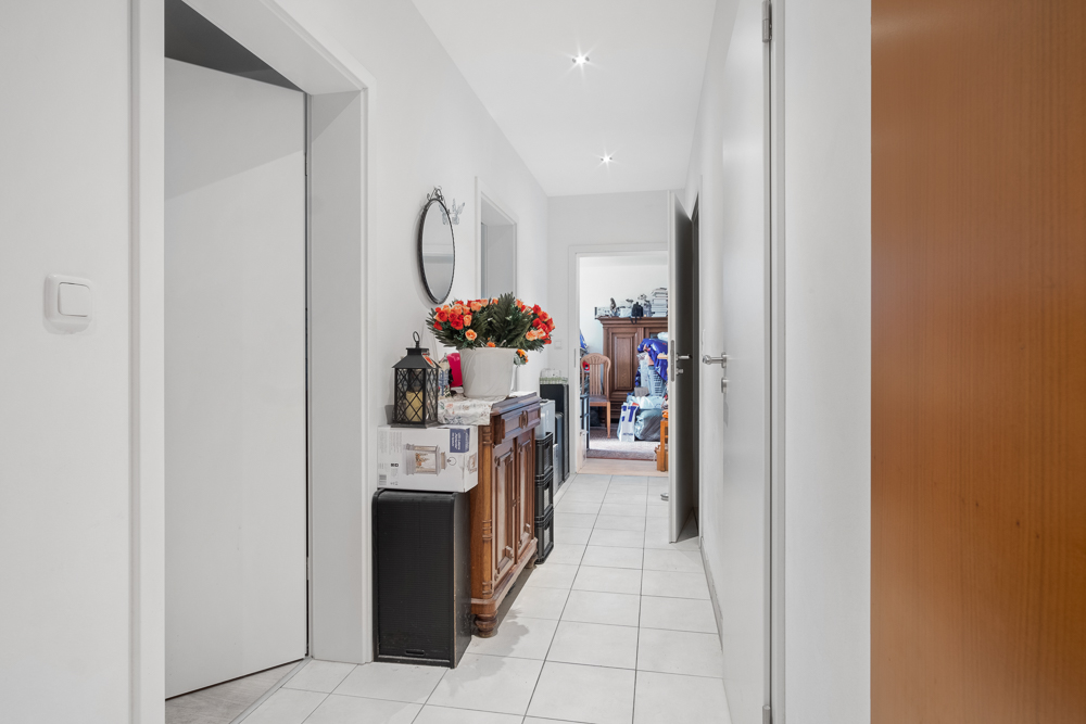 Heller Flur mit Fliesenboden, Kommode, Blumen und Spiegel an der Wand.