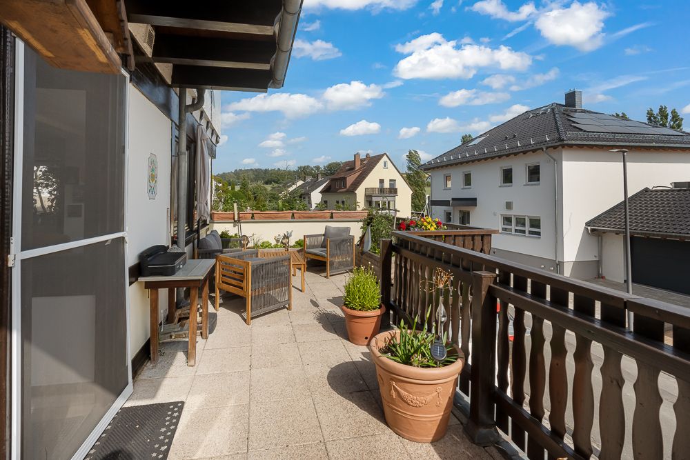 Große Terrasse mit Holzmöbeln, Pflanzen in Töpfen und Blick auf Nachbarhäuser.
