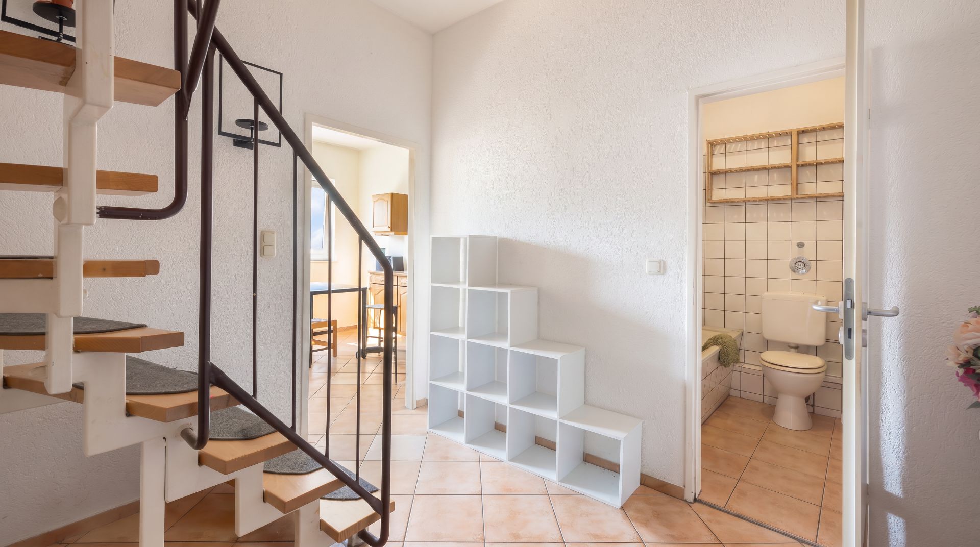 Heller Flur mit Wendeltreppe, Regalen und Blick ins Badezimmer mit Toilette.