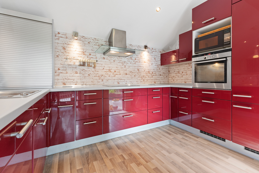 Moderne Küche mit roten Hochglanzfronten, weißen Arbeitsplatten und heller Holzboden.