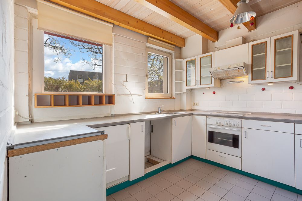 Helle Küche mit weißen Schränken, Fenstern, Herd und sichtbaren Holzbalken an der Decke.