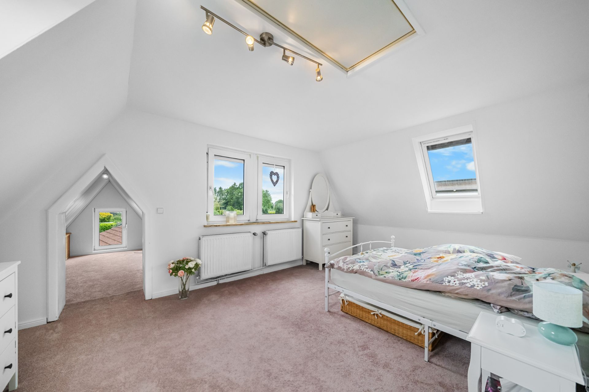 Helles Schlafzimmer mit Dachfenster, Bett, Kommode und Teppichboden.