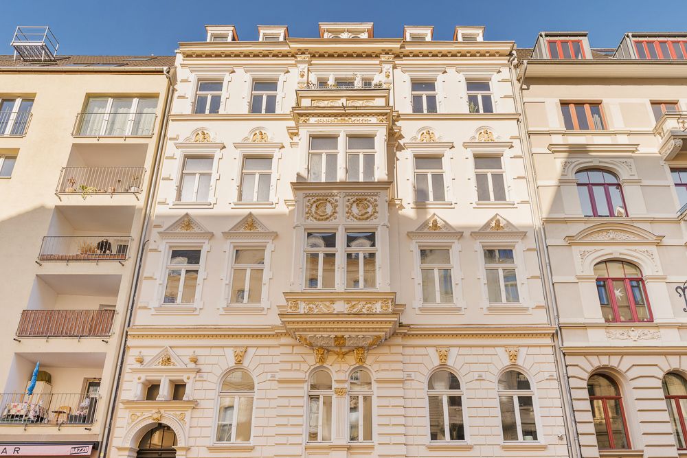 Fassade eines hellen Wohngebäudes mit vielen Fenstern und goldenen Verzierungen.