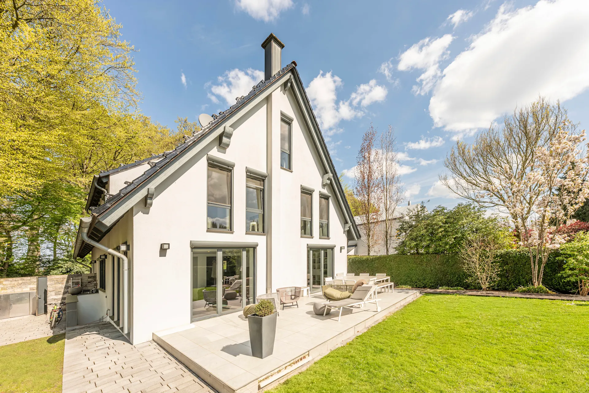 Modernes Einfamilienhaus mit Terrasse und großem Garten bei sonnigem Wetter.
