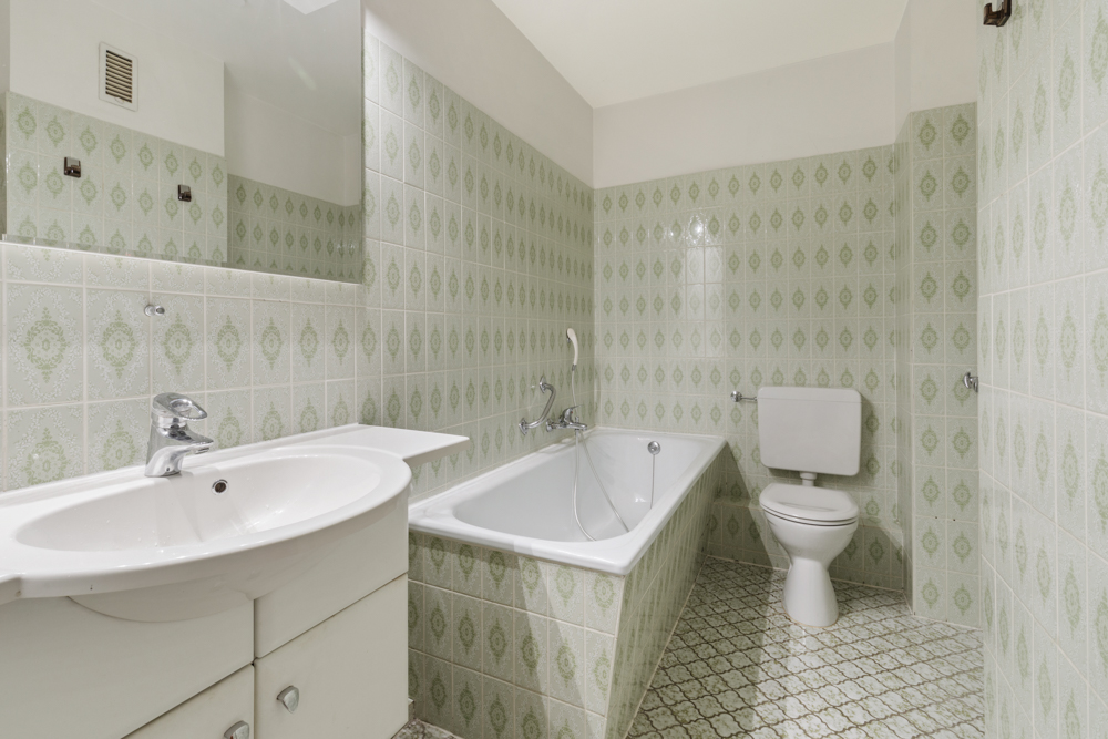 Badezimmer mit Badewanne, Waschbecken und Toilette, grüne gemusterte Fliesen an Wand und Boden.