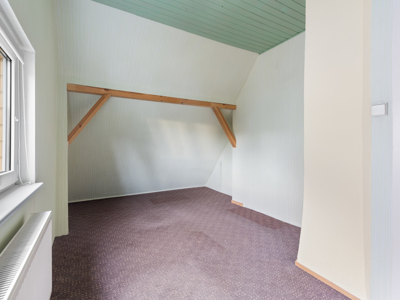 Leerer Dachraum mit schrägen Wänden, Fenster links und grün gestrichener Decke.