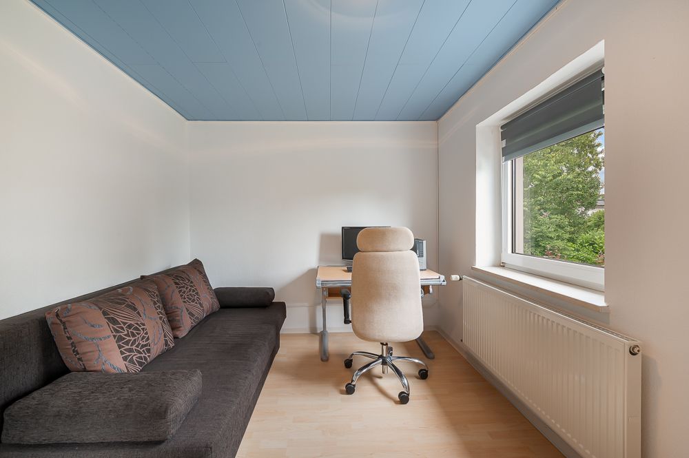 Kleines Zimmer mit Schreibtisch, Bürostuhl, Sofa und Fenster mit Blick ins Grüne.